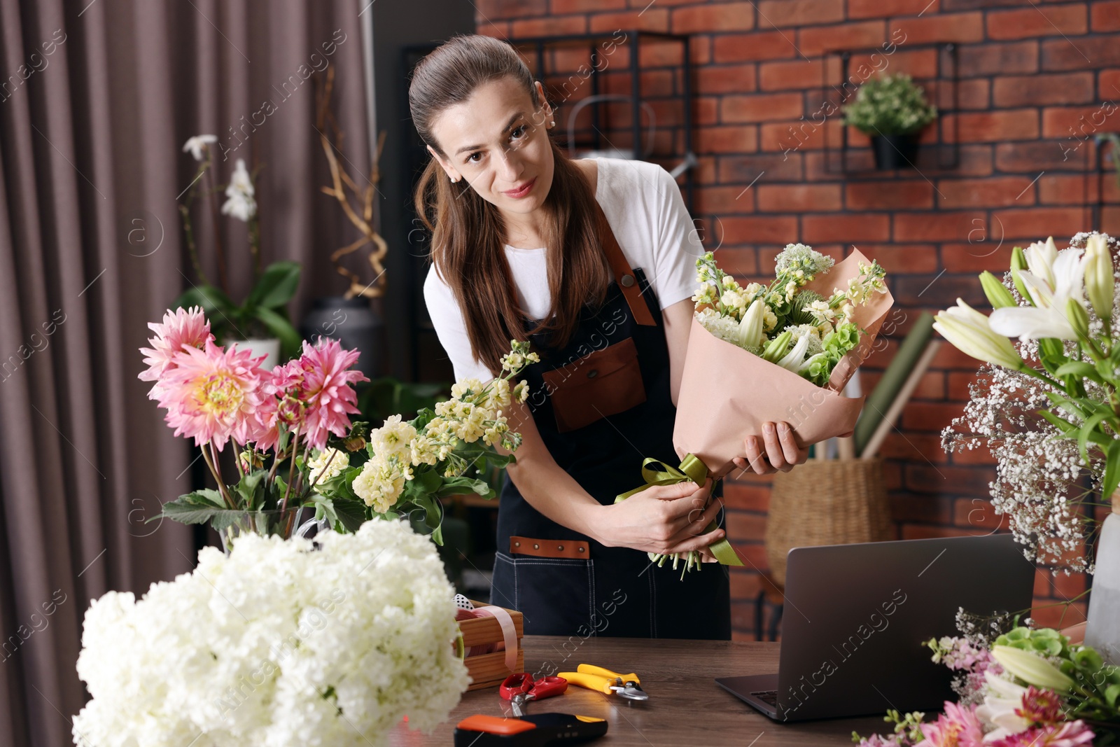 Professional florist making bouquet of flowers at wooden table in shop Photo of Professional florist making bouquet of flowers at wooden table in shop