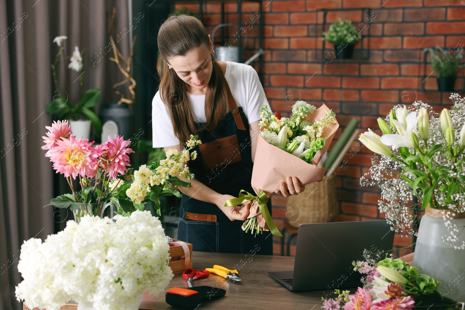 Professional florist making bouquet of flowers at wooden table in shop Photo of Professional florist making bouquet of flowers at wooden table in shop