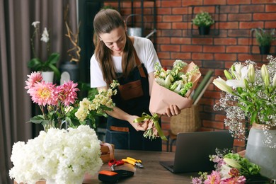 Photo of Professional florist making bouquet of flowers at wooden table in shop