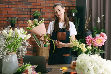 Photo of Professional florist making bouquet of flowers at wooden table in shop