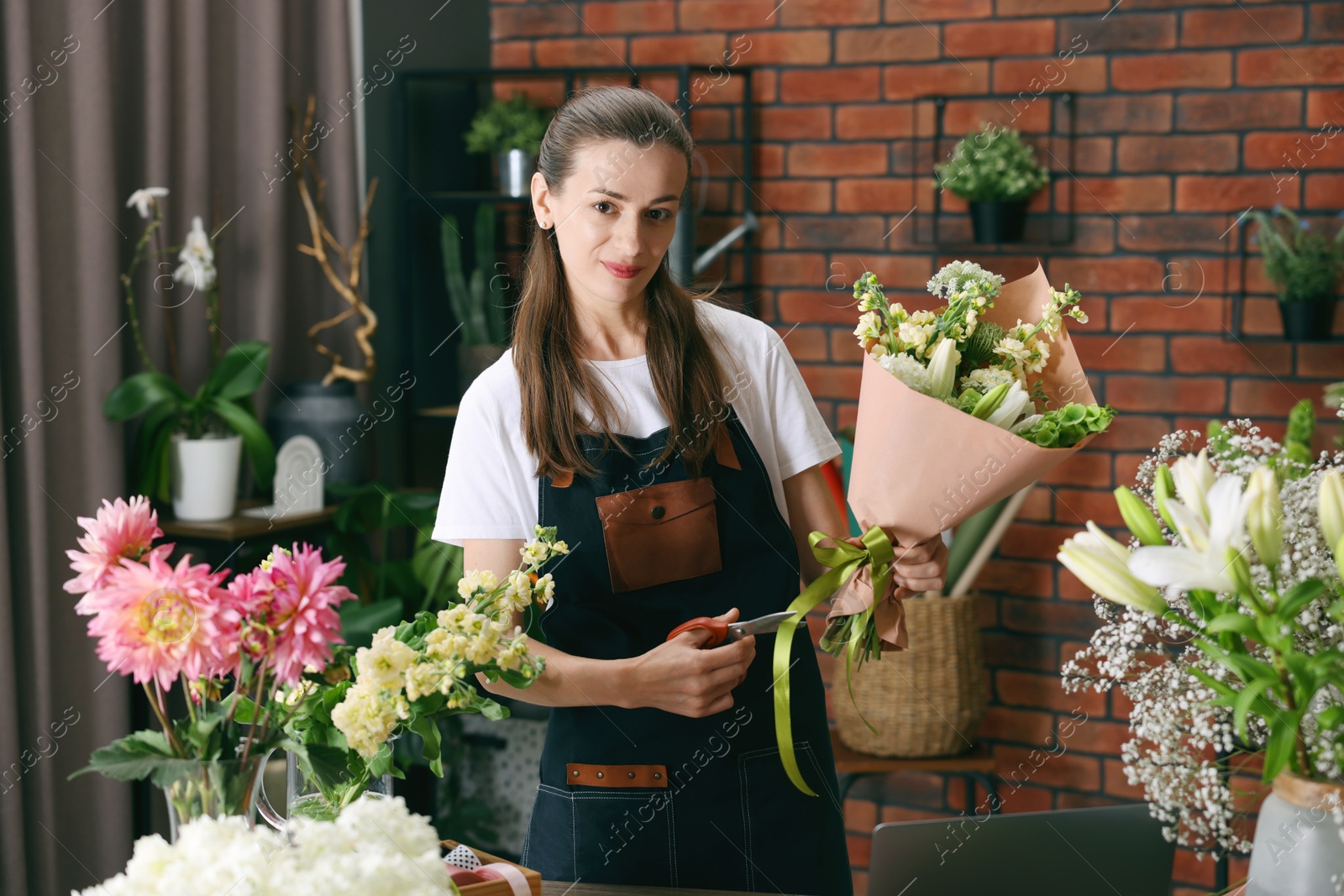 Photo of Professional florist making bouquet of flowers at wooden table in shop