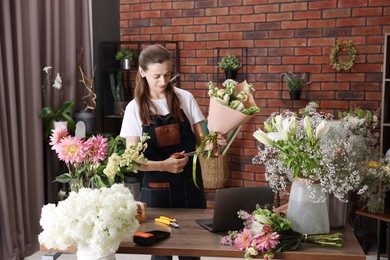 Photo of Professional florist making bouquet of flowers at wooden table in shop
