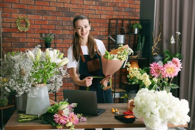 Photo of Professional florist making bouquet of flowers at wooden table in shop