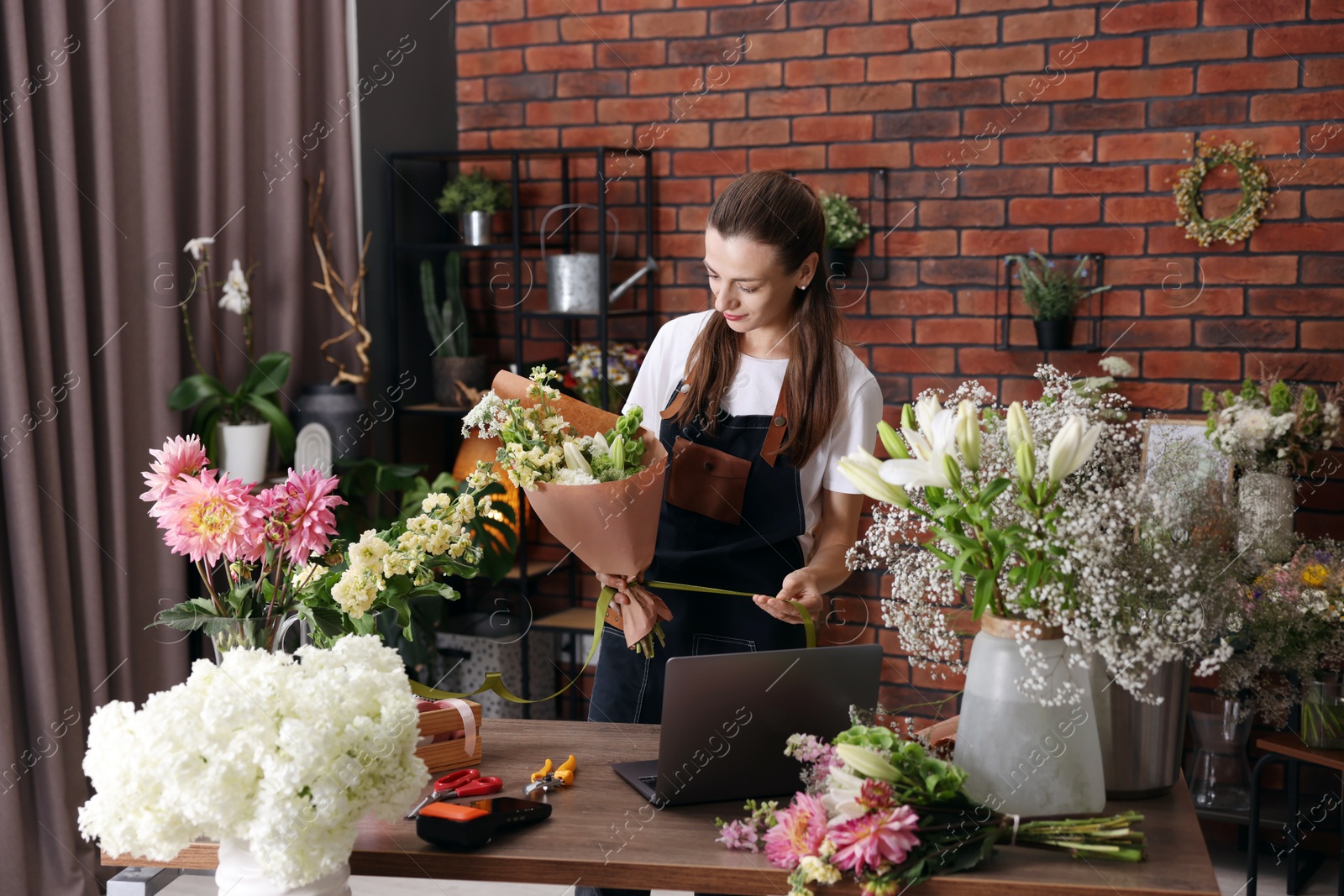 Professional florist making bouquet of flowers at wooden table in shop Photo of Professional florist making bouquet of flowers at wooden table in shop