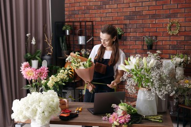 Photo of Professional florist making bouquet of flowers at wooden table in shop