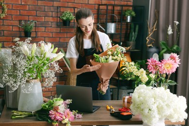 Photo of Professional florist making bouquet of flowers at wooden table in shop