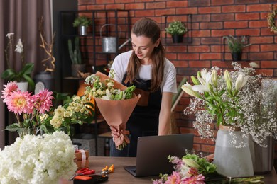 Photo of Professional florist making bouquet of flowers at wooden table in shop