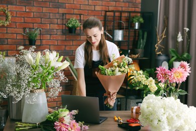 Photo of Professional florist making bouquet of flowers at wooden table in shop