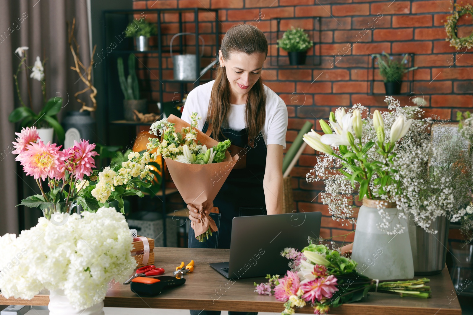 Photo of Professional florist making bouquet of flowers at wooden table in shop