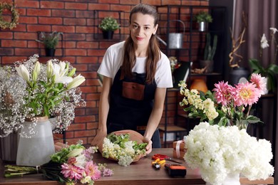 Photo of Professional florist making bouquet of flowers at wooden table in shop