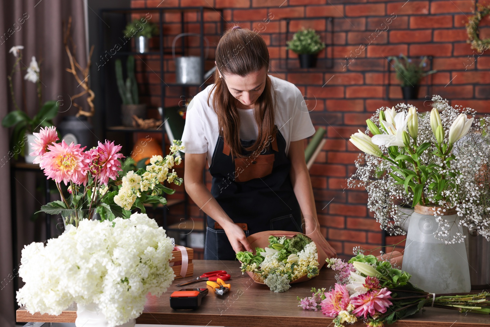 Professional florist making bouquet of flowers at wooden table in shop Photo of Professional florist making bouquet of flowers at wooden table in shop