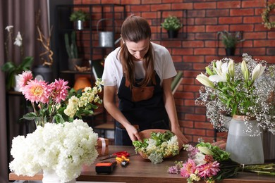 Photo of Professional florist making bouquet of flowers at wooden table in shop