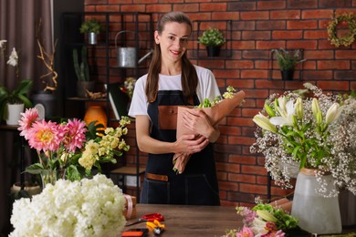 Photo of Professional florist making bouquet of flowers at wooden table in shop