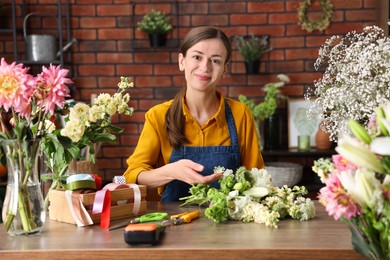 Photo of Professional florist making bouquet of flowers at wooden table in shop