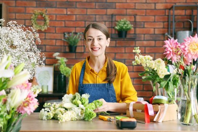 Photo of Professional florist making bouquet of flowers at wooden table in shop