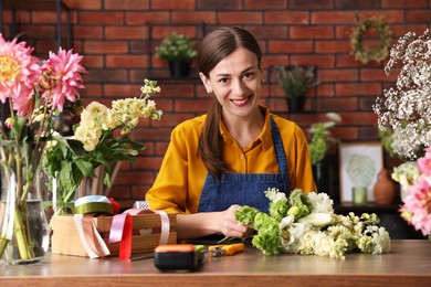 Photo of Professional florist making bouquet of flowers at wooden table in shop