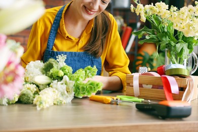 Photo of Professional florist making bouquet of flowers at wooden table in shop, closeup
