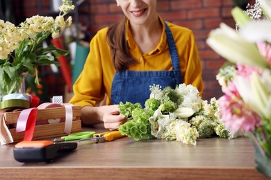 Photo of Professional florist making bouquet of flowers at wooden table in shop, closeup