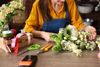 Photo of Professional florist making bouquet of flowers at wooden table in shop, closeup