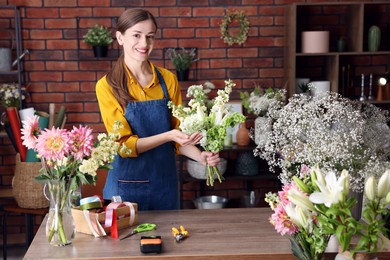 Photo of Professional florist making bouquet of flowers at wooden table in shop