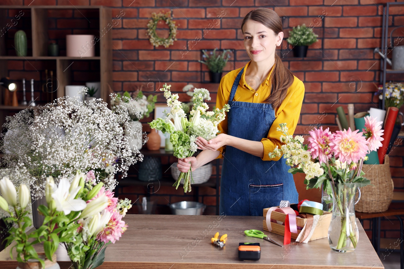Photo of Professional florist making bouquet of flowers at wooden table in shop