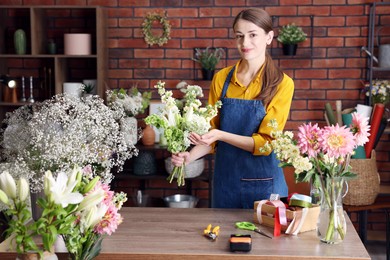 Photo of Professional florist making bouquet of flowers at wooden table in shop