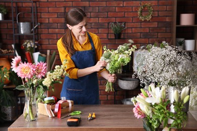 Photo of Professional florist making bouquet of flowers at wooden table in shop