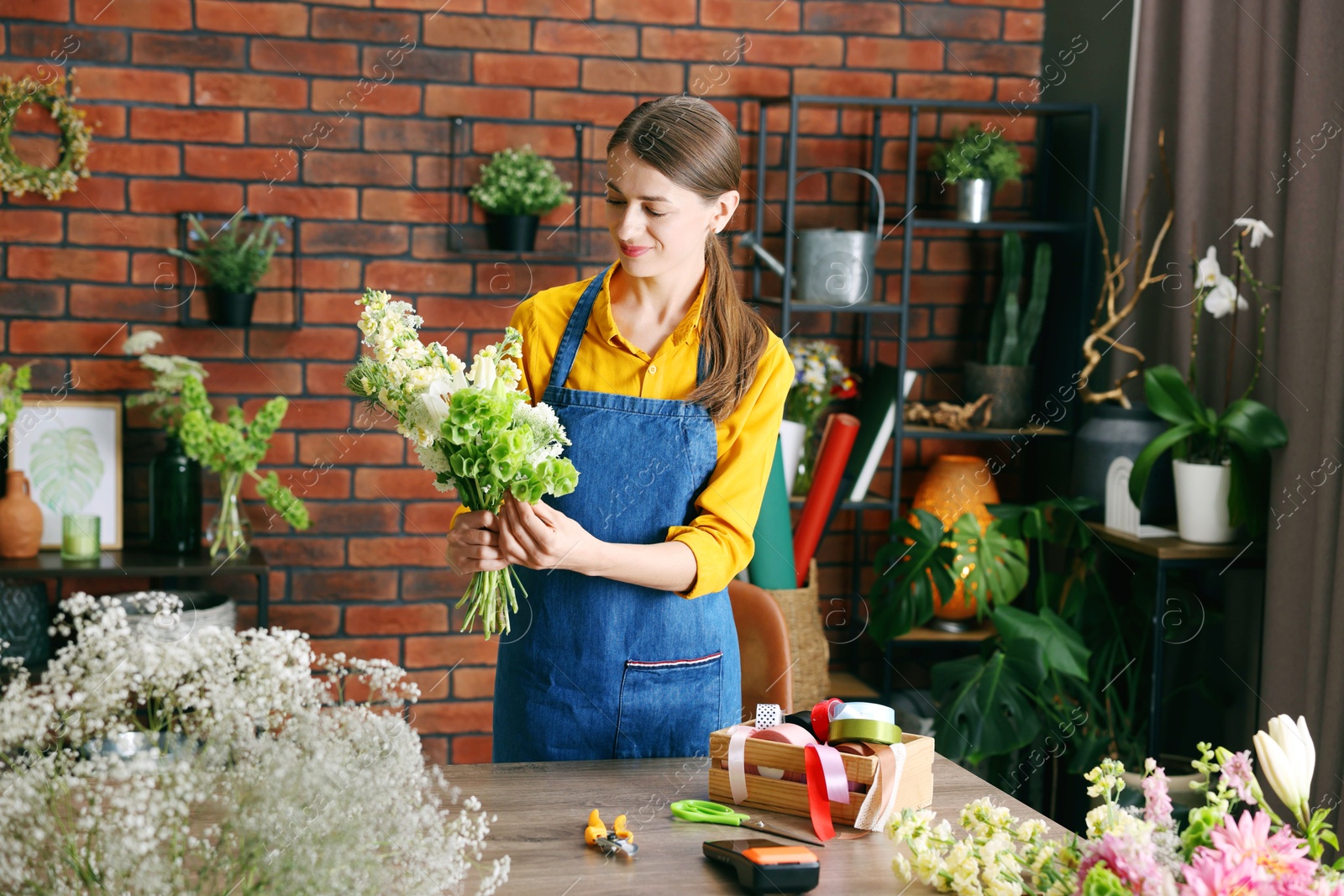 Photo of Professional florist making bouquet of flowers at wooden table in shop