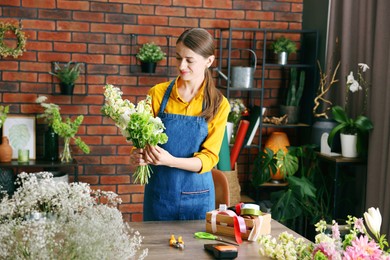 Photo of Professional florist making bouquet of flowers at wooden table in shop