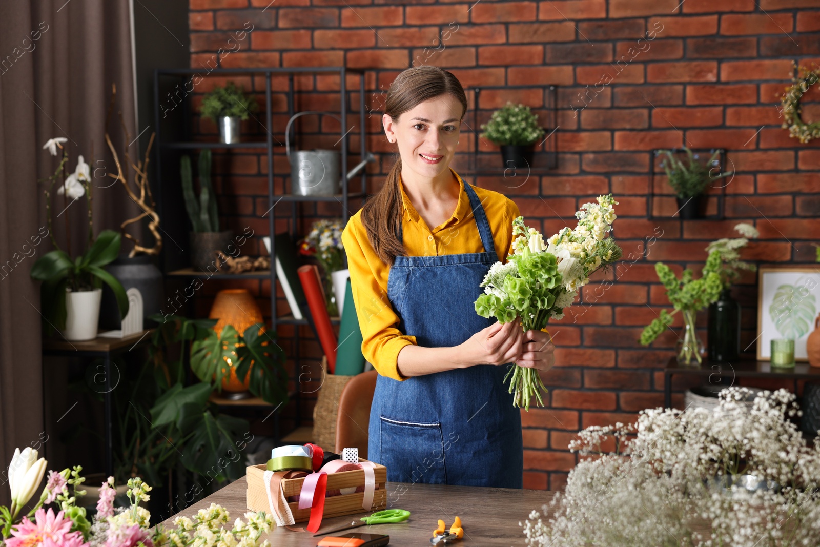 Photo of Professional florist making bouquet of flowers at wooden table in shop