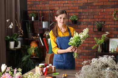 Photo of Professional florist making bouquet of flowers at wooden table in shop