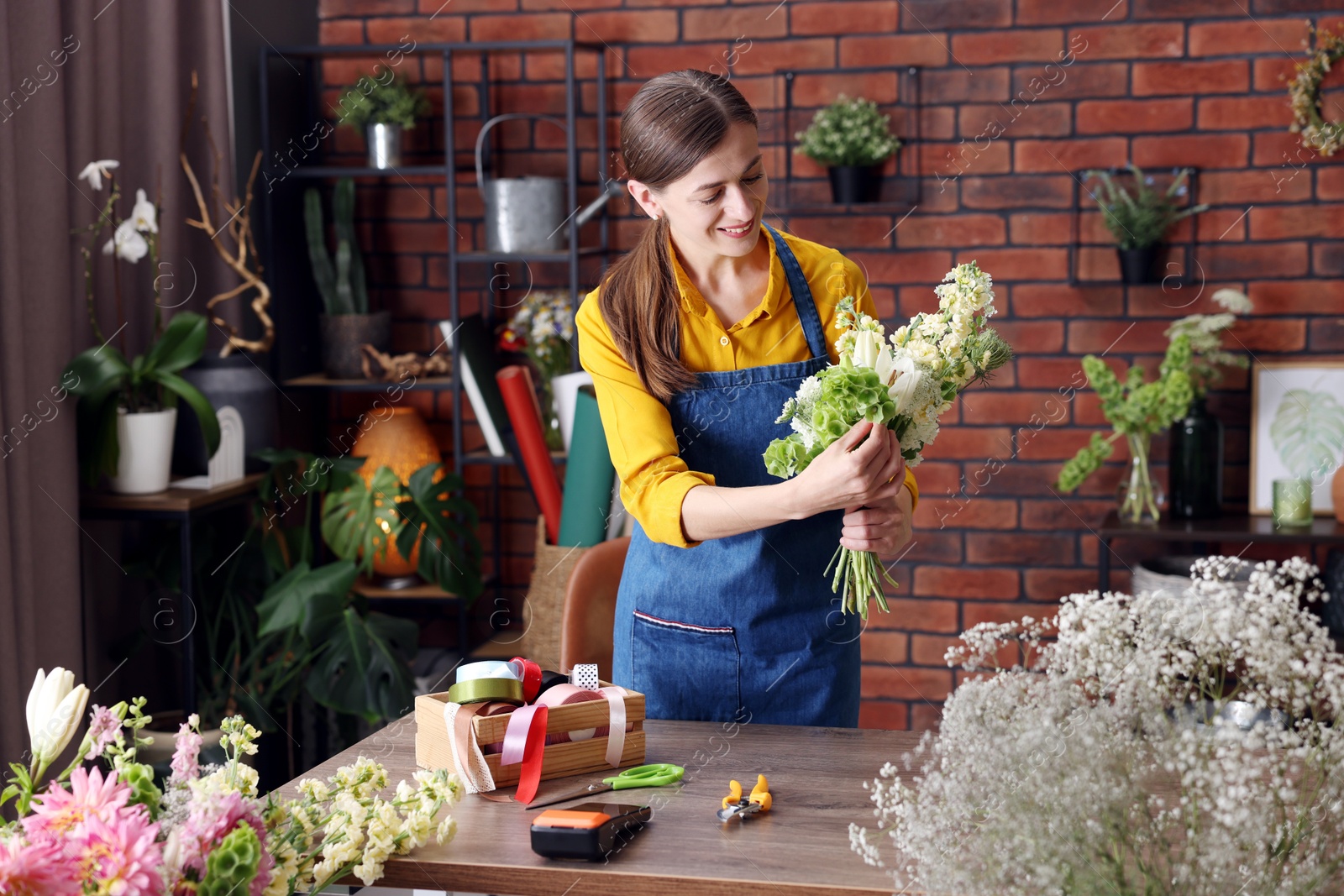 Photo of Professional florist making bouquet of flowers at wooden table in shop