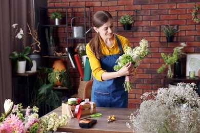 Photo of Professional florist making bouquet of flowers at wooden table in shop