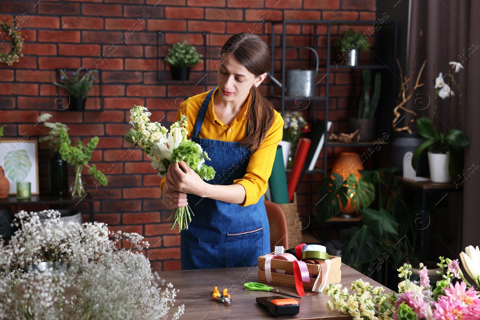 Photo of Professional florist making bouquet of flowers at wooden table in shop