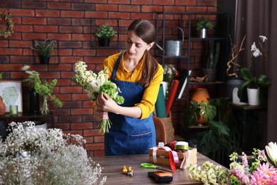 Photo of Professional florist making bouquet of flowers at wooden table in shop