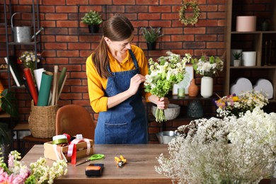 Photo of Professional florist making bouquet of flowers at wooden table in shop