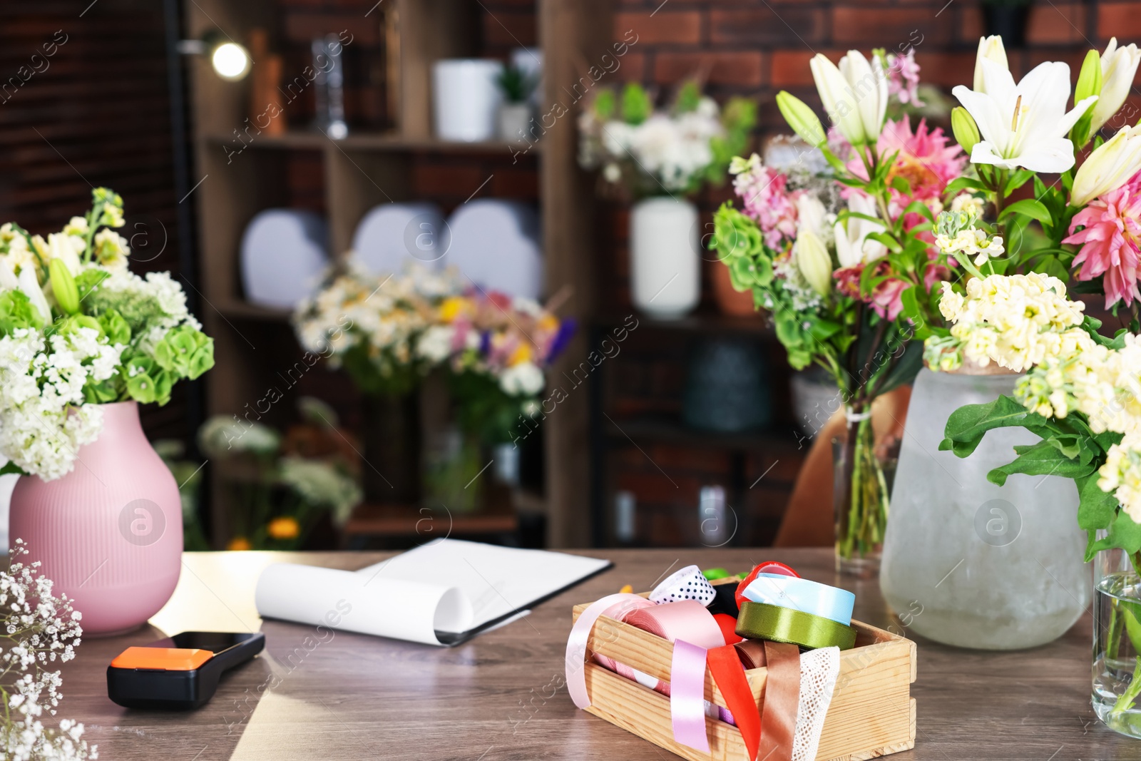 Photo of Beautiful flowers, ribbons and other tools on wooden table in florist's shop