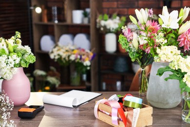 Photo of Beautiful flowers, ribbons and other tools on wooden table in florist's shop
