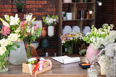 Photo of Beautiful flowers, ribbons and other tools on wooden table in florist's shop