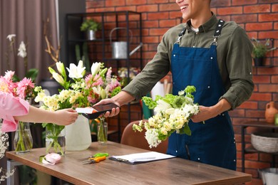 Photo of Florist with bouquet of flowers taking payment from client via terminal in shop, closeup
