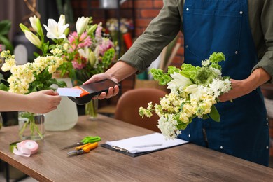 Photo of Florist with bouquet of flowers taking payment from client via terminal in shop, closeup