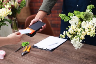 Photo of Florist with bouquet of flowers taking payment from client via terminal in shop, closeup