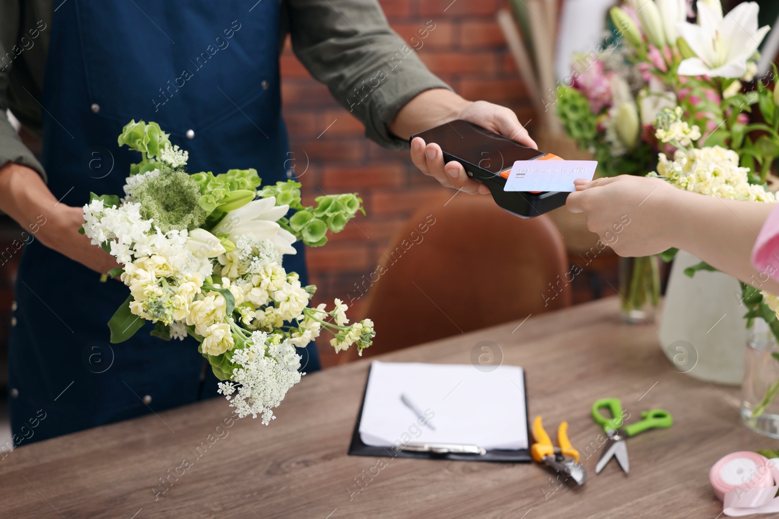 Photo of Florist with bouquet of flowers taking payment from client via terminal in shop, closeup