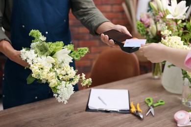 Photo of Florist with bouquet of flowers taking payment from client via terminal in shop, closeup