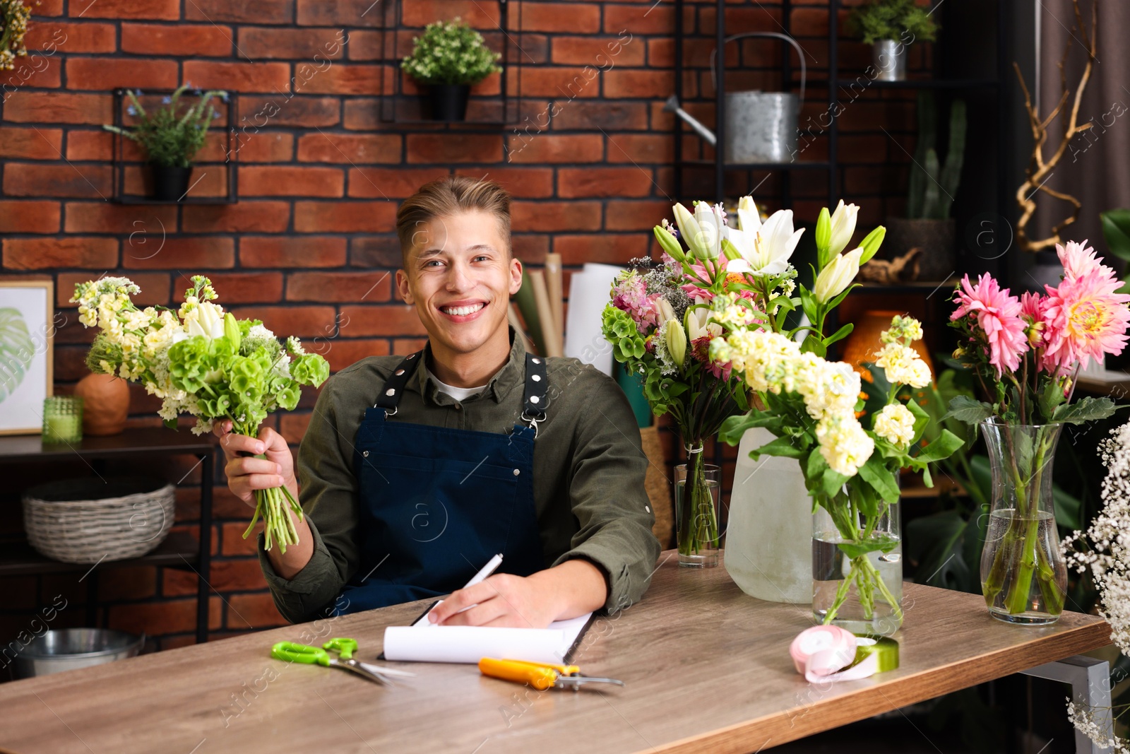 Photo of Professional florist with bouquet of flowers working at wooden table in shop