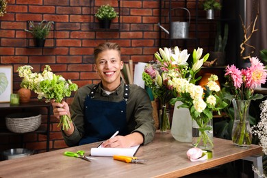 Photo of Professional florist with bouquet of flowers working at wooden table in shop