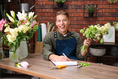 Photo of Professional florist with bouquet of flowers working at wooden table in shop
