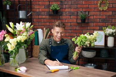 Photo of Professional florist with bouquet of flowers working at wooden table in shop