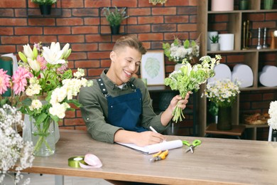 Photo of Professional florist with bouquet of flowers working at wooden table in shop