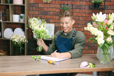 Photo of Professional florist with bouquet of flowers working at wooden table in shop